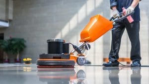 Personale di impresa di pulizie al lavoro con macchina monospazzola per la lucidatura di pavimenti