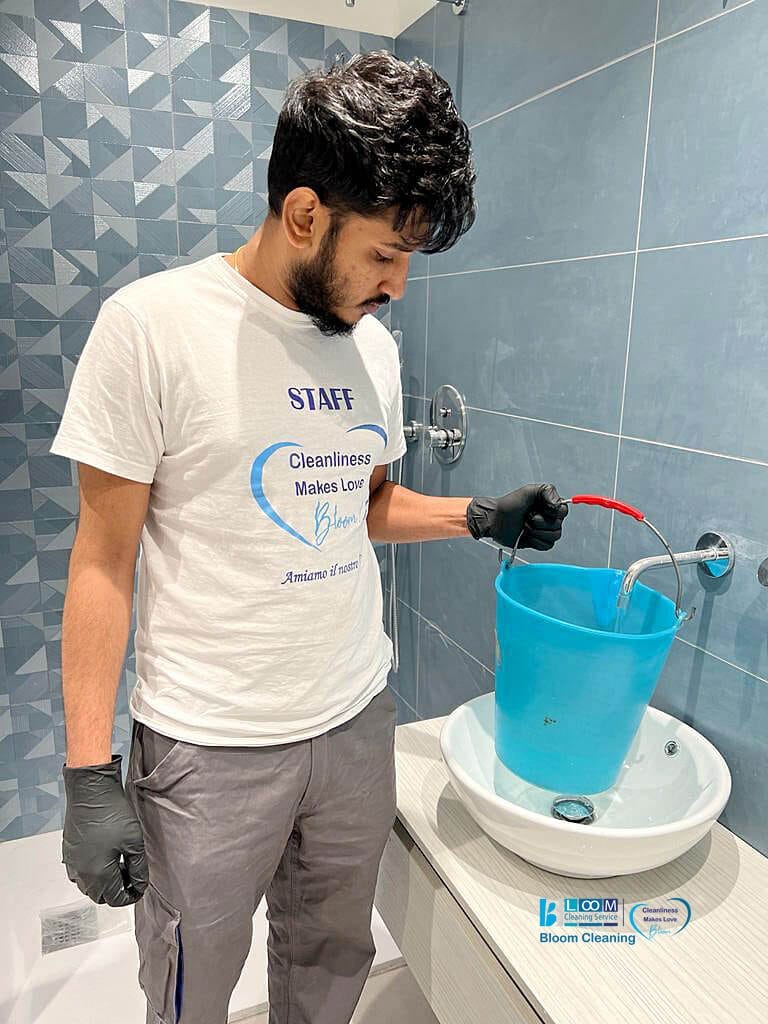 Un uomo del Bloom Cleaning Service pulisce un secchio blu in un bagno dopo una pulizia post-cantiere.