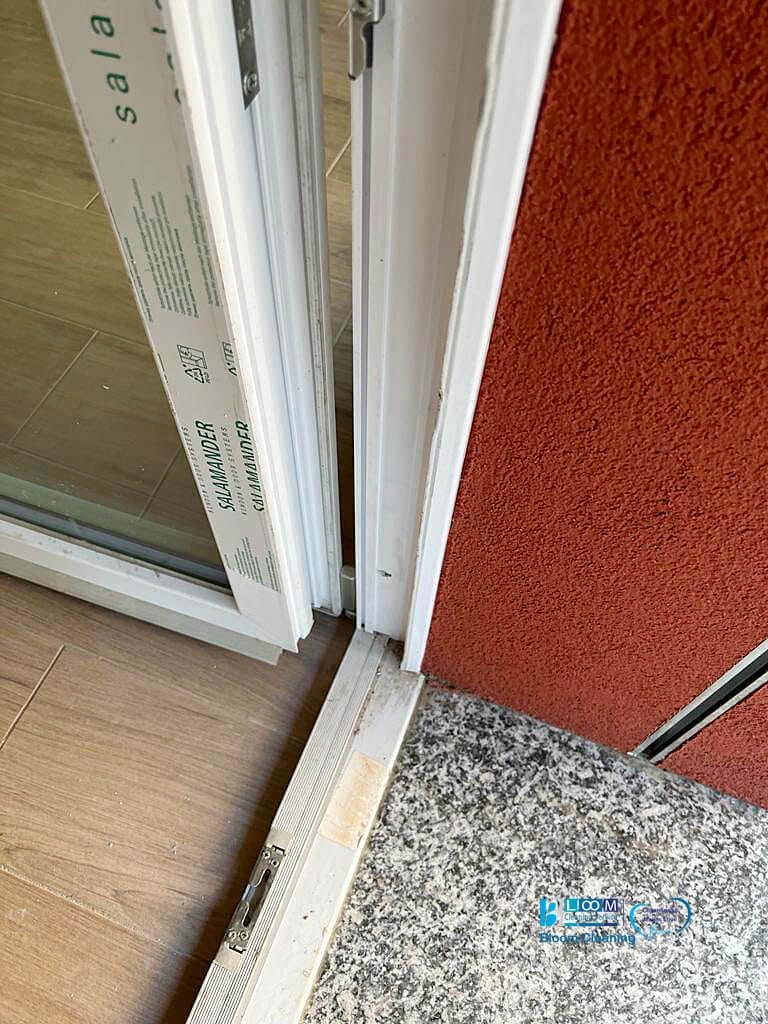 Una porta scorrevole in vetro con telaio bianco e pavimento rosso in una pulizia post-costruzione a Milano.