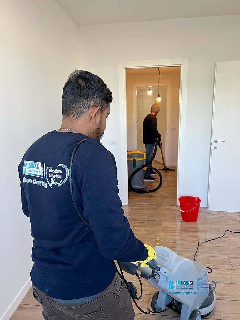 Benvenuto! Un uomo di Bloom Cleaning Service sta eseguendo diligentemente la Pulizia Post-Cantiere in una stanza, pulendo con perizia il pavimento in legno.