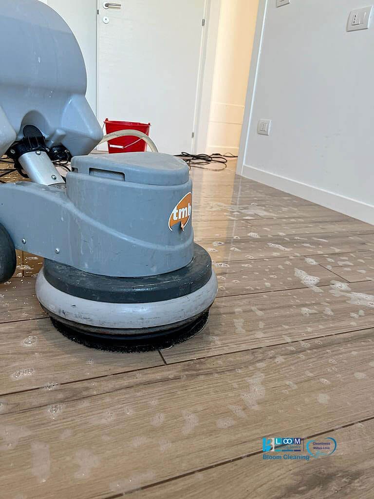 Una persona della Bloom Cleaning Service utilizza una macchina per pulire un pavimento in legno post-cantiere.