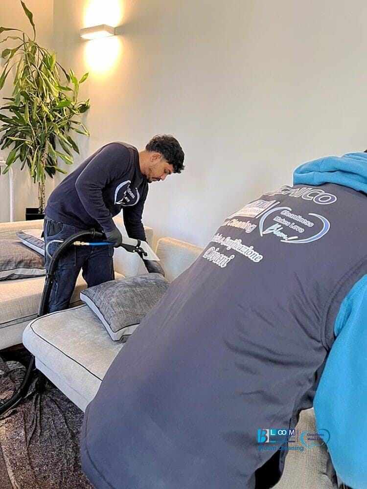 Due uomini puliscono il divano di un soggiorno a Lodi