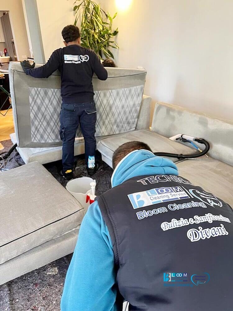 Due uomini stanno pulendo un divano in un soggiorno utilizzando i servizi Bloom Cleaning.