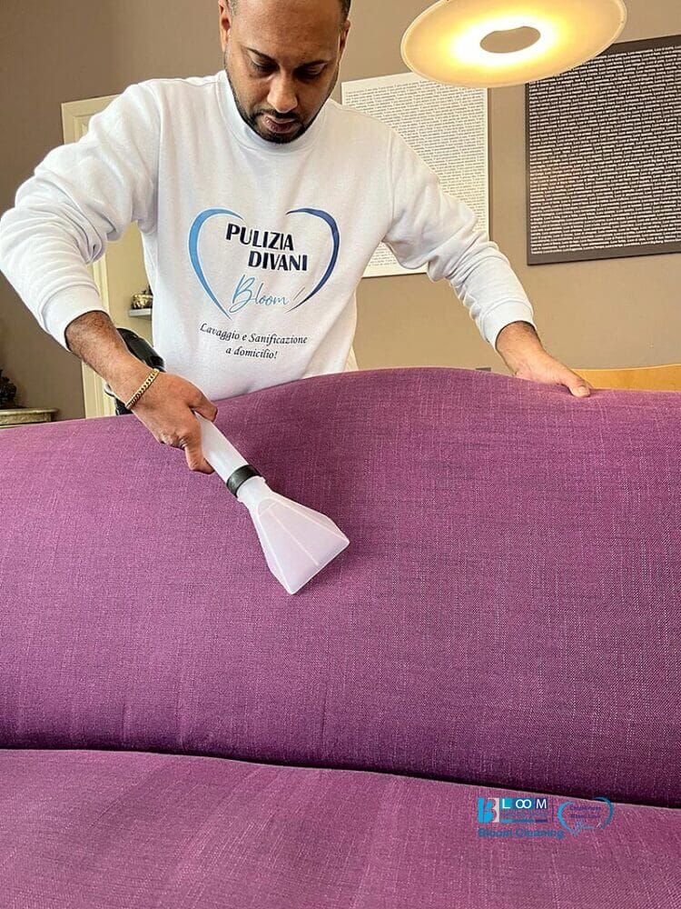Un uomo che pulisce con una spazzola un divano viola in casa a Pavia.