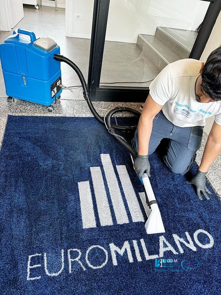 Un uomo che utilizza il Metodo Iniezione/Estrazione per pulire un tappeto blu con il logo Euromilano.