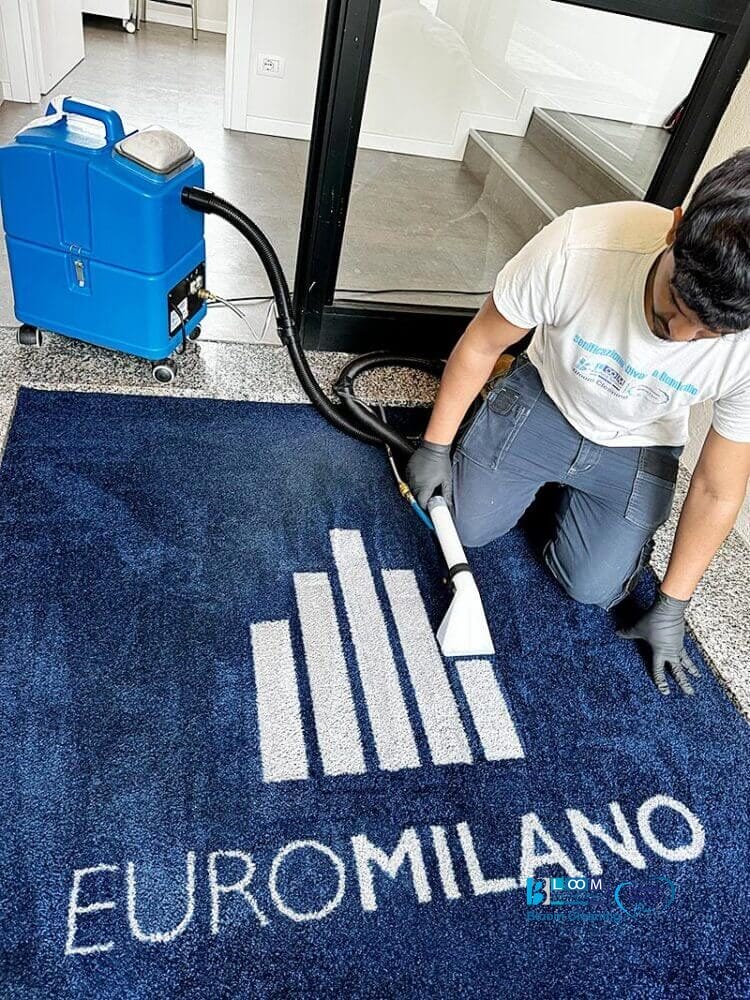 Un uomo sta usando il Metodo Iniezione/Estrazione per pulire un tappeto blu con la scritta euromilano sopra.