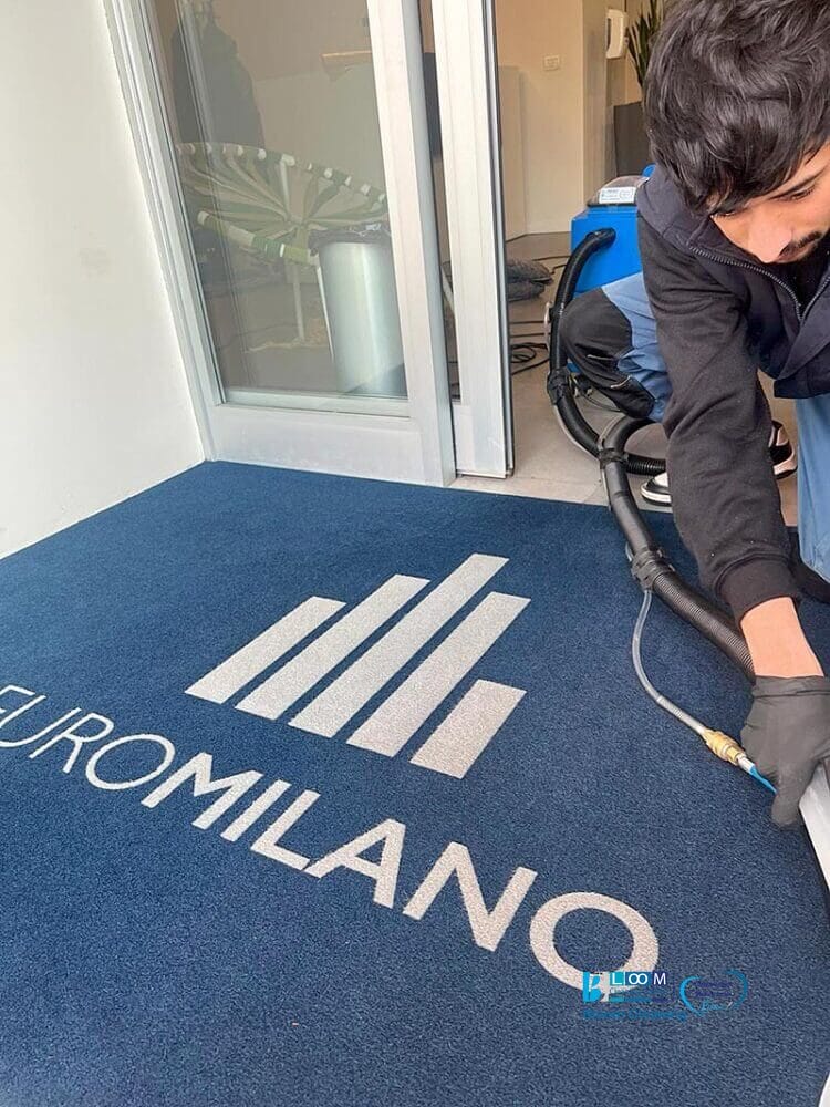 Un uomo che pulisce un tappeto blu con un logo a Milano utilizzando il metodo del Metodo Iniezione/Estrazione.