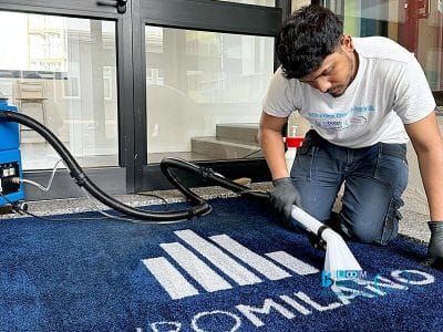 Un uomo pulisce un tappeto blu con un logo utilizzando il Metodo Iniezione/Estrazione.