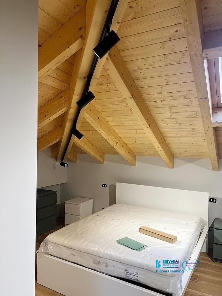 Una camera da letto minimalista con un letto moderno sullo sfondo di un caldo soffitto inclinato in legno e un lucernario che fornisce luce naturale, appena pulita da Bloom Cleaning.