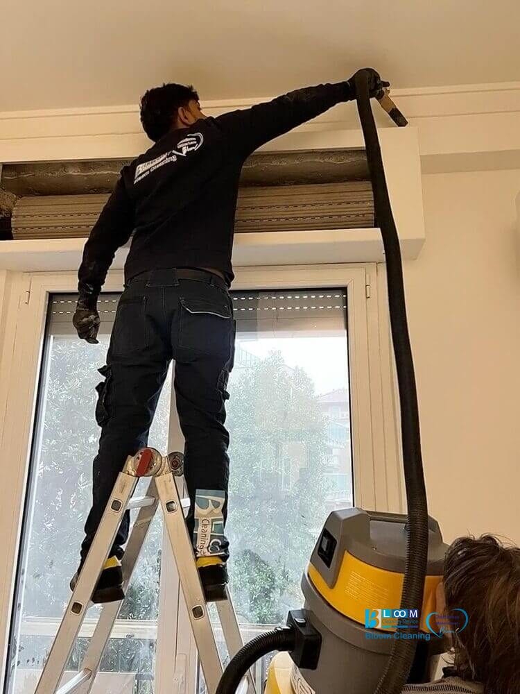 Operaio su scala a pioli che utilizza un tubo aspirante per la pulizia appartamenti, pulisce con esperienza zone alte vicino agli infissi delle finestre a Settimo Milanese.