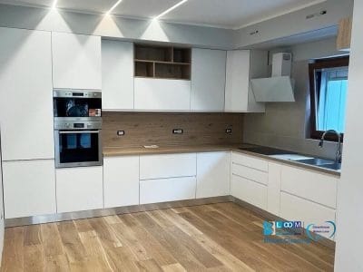 Una cucina moderna con eleganti mobili bianchi, elettrodomestici da incasso e accenti in legno dopo il servizio di pulizie post cantiere di Bloom Cleaning.
