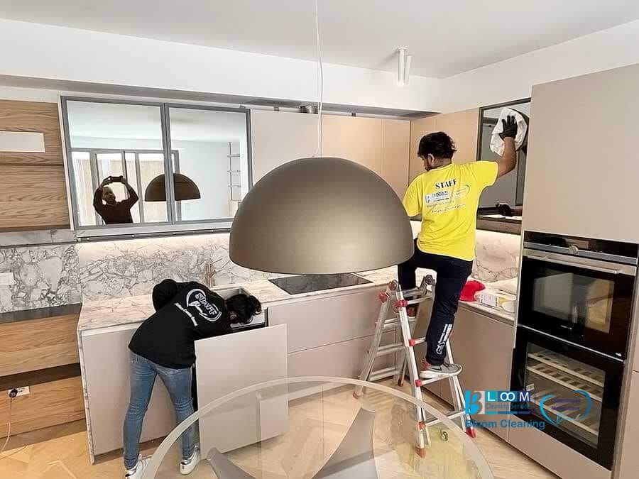 Due individui effettuano la pulizia appartamenti Milano in una cucina moderna, uno in piedi su una scala e l'altro inclinato sul bancone.