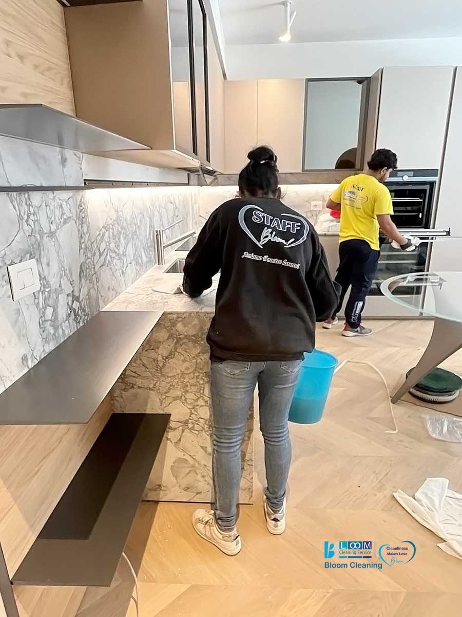 Due individui in una cucina, uno si occupa della pulizia del piano di lavoro mentre l'altro è al lavoro vicino al forno.