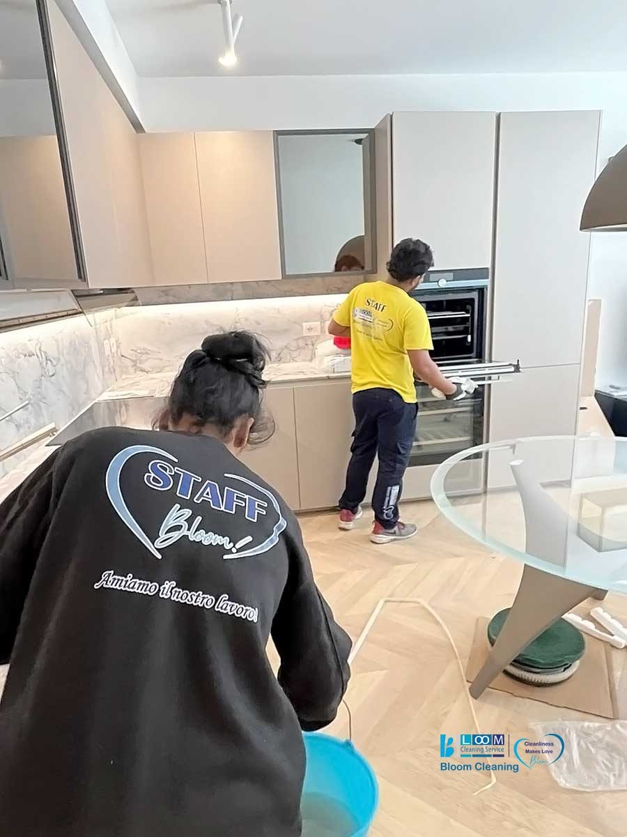 Due individui che indossano magliette "staff" lavorano in un ambiente di cucina moderna, specializzati nella pulizia appartamenti Milano.