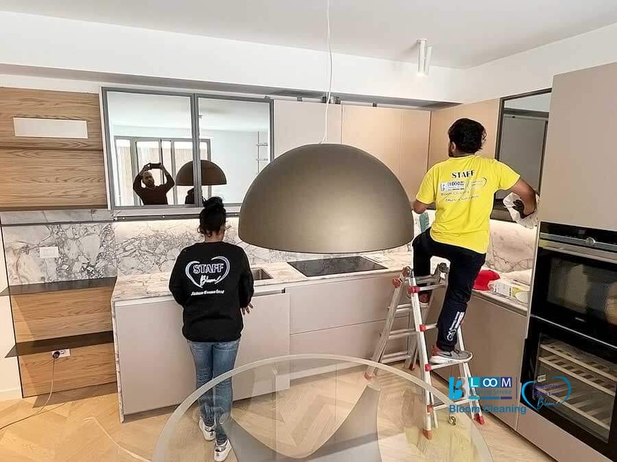 Due membri dello staff che installano una lampada a sospensione in una moderna cucina, eseguendo anche la pulizia degli appartamenti a Milano.