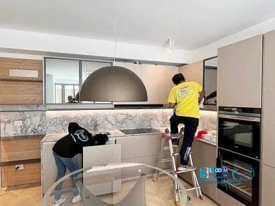 Due persone che puliscono i mobili di una cucina moderna, garantendo la pulizia appartamenti Milano prezzi.