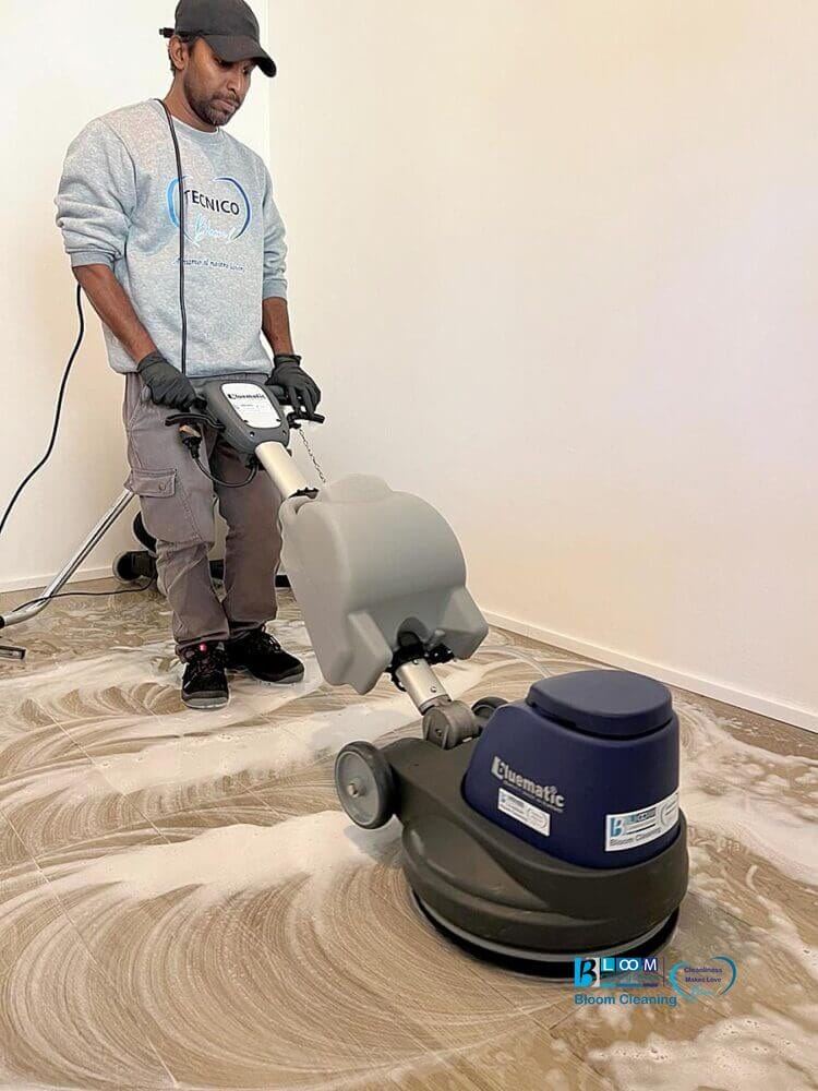Un uomo che utilizza una monospazzola professionale per pulire e lucidare un pavimento in gres porcellanato in un appartamento a Milano dopo il cantiere.