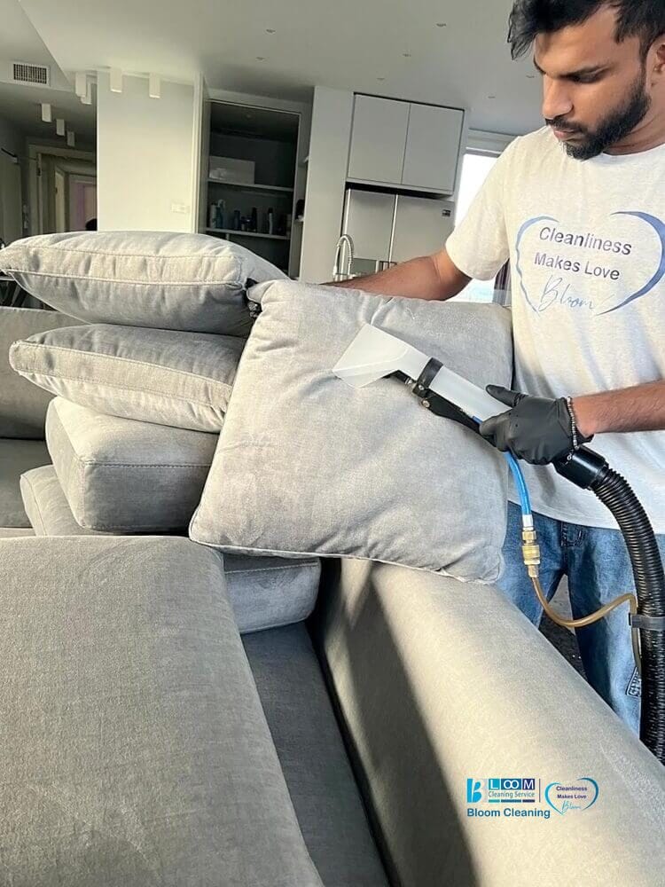 Una persona che indossa i guanti usa un aspirapolvere su una pila di cuscini grigi in un salotto moderno, dimostrando l'efficienza del servizio di lavaggio divani domicilio Segrate di Bloom Cleaning.