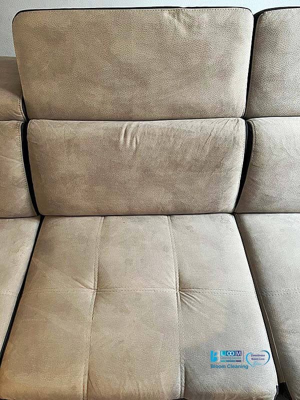 Una vista ravvicinata di un divano componibile imbottito beige con cinque cuscini a vista, caratterizzati da sottili pieghe e dettagli di cucitura. Per una manutenzione impeccabile, rivolgiti agli esperti di Bloom Cleaning in Pulizia Divani a Domicilio ad Assago.