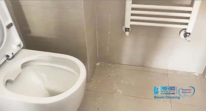 Un bagno con il pavimento ricoperto di detriti vicino a un water bianco e un portasciugamani a parete, ma con i servizi di Bloomcleaning puoi trasformarlo in un santuario immacolato.