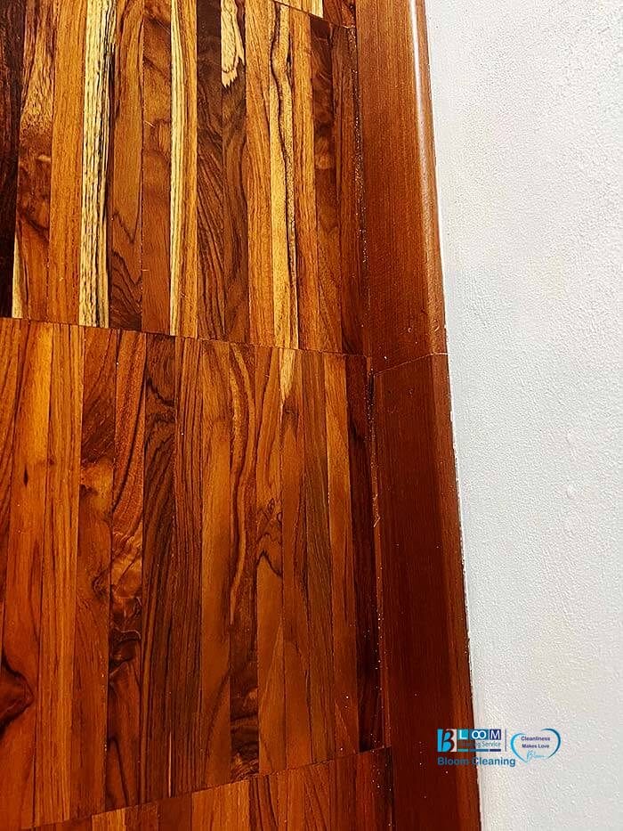 Primo piano di un pavimento in legno lucidato e di uno zoccolo accanto a una parete bianca, che mette in risalto la consistenza e le venature del legno; perfetto per mettere in mostra gli impeccabili risultati dei servizi di pulizia Bloomcleaning.