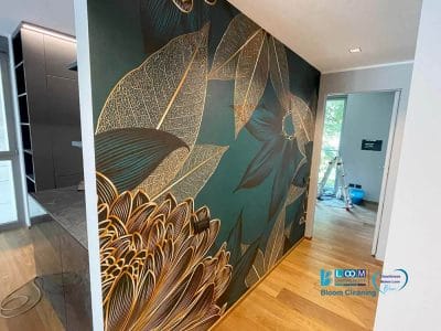 Un corridoio con un grande murale con intricati disegni floreali nei toni dell'oro e del verde scuro. Le foglie e i fiori dettagliati del murale creano un punto focale sorprendente, che ricorda la Bozza automatica. È visibile una stanza adiacente.