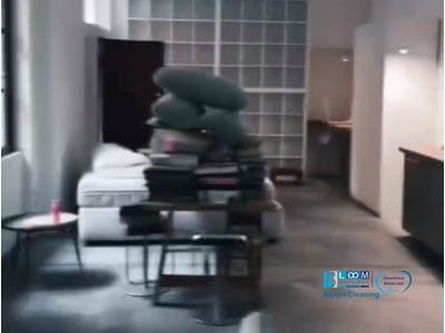 Un loft moderno a Milano con una parete in vetro, una cucina attrezzata e una pila di cuscini e libri su un tavolo centrale. Lo spazio è mantenuto immacolato con l'aiuto di Pulizia Professionale.