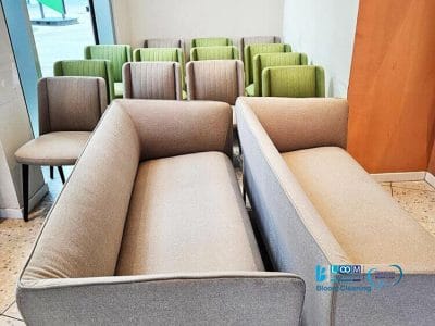 File di sedie verdi e due divani grigio chiaro sono disposti in una stanza con una finestra che si affaccia sull'esterno, gestita dagli esperti servizi di lavaggio sedie imbottite di Bloom Cleaning.