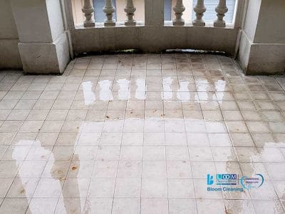 Un balcone con pavimento piastrellato mostra i segni della pioggia, evidenti nelle pozze d'acqua che riflettono la balaustra e gli edifici vicini nella zona Moscova di Milano.