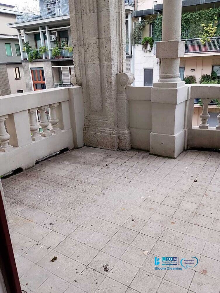 Un balcone piastrellato con ringhiere in pietra si affaccia su una strada residenziale di Milano Zona Moscova, fiancheggiata da edifici adornati di verde.