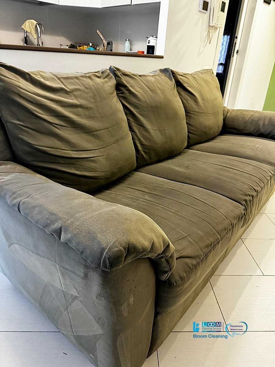 Un divano in tessuto verde a tre posti è posizionato su un pavimento piastrellato, con una cucina automatica Bozza visibile sullo sfondo.