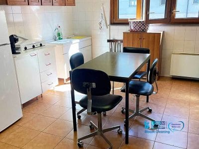 Una cucina con mobili in legno e un elegante paraschizzi piastrellato bianco esalta l'aspetto moderno. Include un frigorifero, un lavandino e un tavolo rettangolare con quattro sedie girevoli. Ampie finestre permettono alla luce naturale di illuminare lo spazio, creando un'atmosfera invitante che è sia funzionale che bozza automatica.