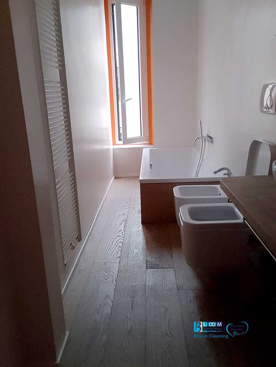 Il bagno minimalista è dotato di pavimento in legno, vasca da bagno, bidet e water. Una finestra alta e stretta impreziosisce la parete più lontana, aggiungendo un tocco di serenità all'atmosfera e invitando la luce naturale: una vera Bozza automatica di elegante semplicità.