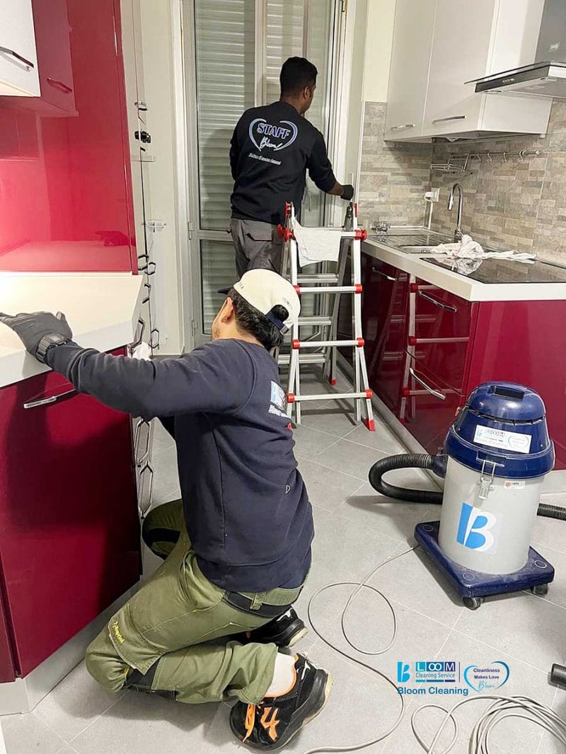 Due operai in cucina, uno che sistema un piano di lavoro e l'altro su una scala che ripara le persiane. Un aspirapolvere e degli utensili sono visibili sul pavimento, a dimostrazione dell'attenzione al dettaglio che contraddistingue Pulizia Professionale quando si occupa della manutenzione di Appartamenti eleganti come quelli di San Babila Milano.