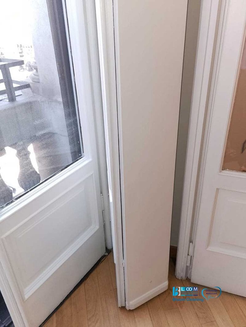 Uno stretto mobiletto portaoggetti si incastra tra una porta in vetro e una porta interna bianca su un pavimento in legno, completando alla perfezione il fascino dell'Appartamento durante la Pulizia Straordinaria.