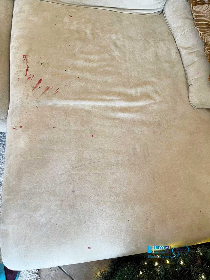 Un divano beige con macchie rosse e uno scorcio di albero di Natale in basso offre una tela intrigante, che invita a racconti di feste o incidenti.