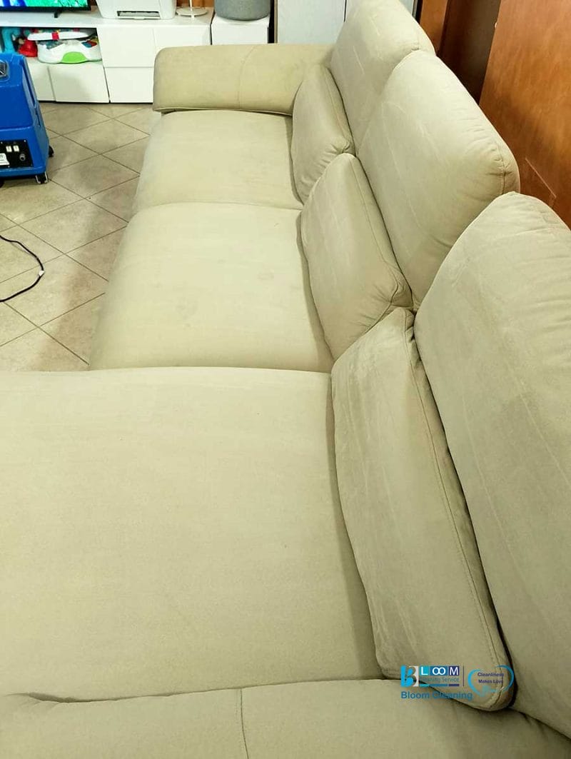 Un divano beige a quattro posti con schienali imbottiti completa l'ambiente piastrellato. Sullo sfondo, una macchina blu aggiunge un tocco moderno, fondendosi perfettamente come un'abile bozza automatica.