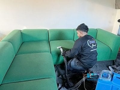 In un accogliente appartamento a Loreto, a Milano, una persona si prende cura meticolosamente del suo divano componibile verde, utilizzando un aspirapolvere per la pulizia dei divani.