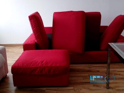 Divano componibile rosso con cuscini staccati e appoggiati allo schienale, su un pavimento in legno lucido nell'elegante Piazza Tricolore di Milano, accanto a un tavolo in metallo con piano in vetro. Il posto perfetto per rilassarsi dopo la routine del lavaggio divani.