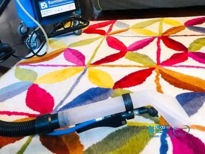 Una macchina per la pulizia dei tappeti dotata di ugello trasparente e tubo flessibile collegato viene abilmente utilizzata su un tappeto multicolore, dimostrando l'efficacia della pulizia professionale attraverso il metodo ad iniezione-estrazione.