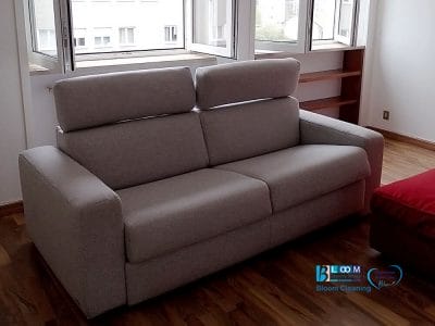 Un divano grigio in una stanza con ampie finestre e pavimento in legno, accanto a un pouf rosso, crea uno spazio invitante. Considerate di fornire elementi decorativi aggiuntivi per una migliore risposta da parte degli ospiti.