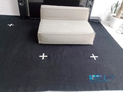 Un sedile beige è appoggiato su un tappeto nero con segni più bianchi, incorniciato da una TV e degli altoparlanti. Sulla destra, un cactus in vaso aggiunge vita a questa accogliente configurazione. L'atmosfera, dal design senza sforzo bozza, sussurra raffinatezza attraverso ogni elemento della sua disposizione.