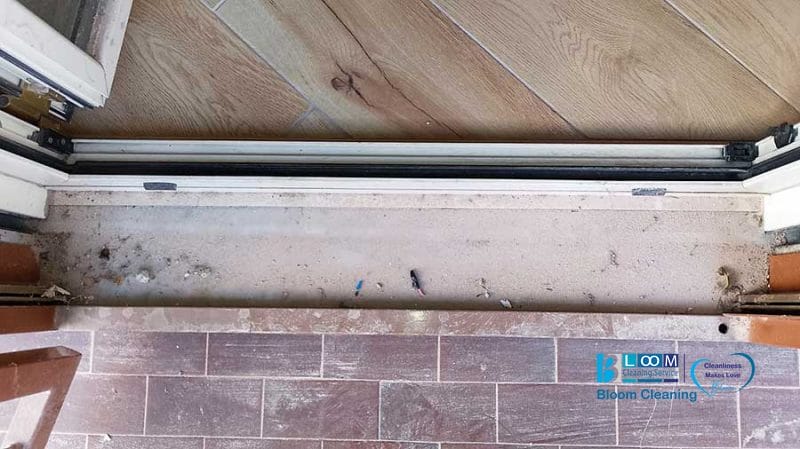 Apri la porta scorrevole con il suo binario e pavimento polverosi, rivelando un pavimento chiaro all'interno che si trasforma in piastrelle scure all'esterno. Per spazi incontaminati nella Zona Lotto di Milano, prendi in considerazione Pulizia Appartamenti per un tocco professionale.