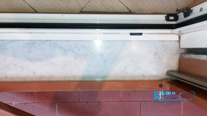 Il davanzale in marmo con motivi bianchi e grigi è incorniciato alla perfezione dai binari di una porta scorrevole e da una sezione di muro in mattoni rossi, risplendenti grazie al tocco meticoloso di Bloom Cleaning.