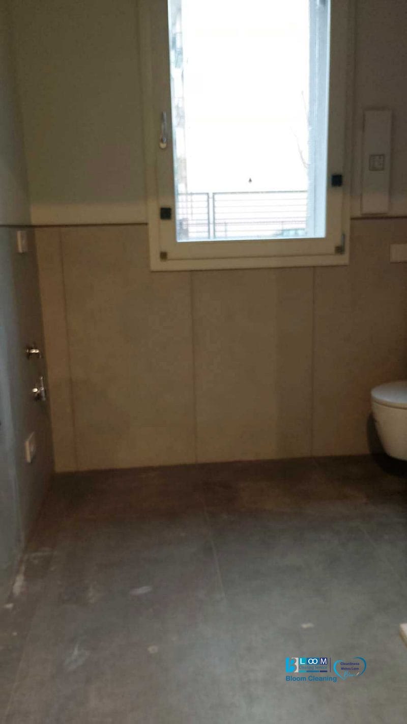 Il bagno semplice nella villetta ad Assago è dotato di piastrelle grigie e una finestra, con uno spazio vuoto per una potenziale installazione. Un water è parzialmente visibile sulla destra, perfetto per un progetto di trasformazione prima e dopo o pulizia post-cantiere.