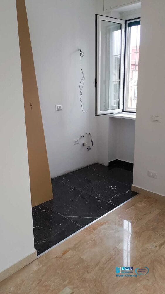 Stanza parzialmente rifinita con pavimento in marmo, una sezione rialzata piastrellata di nero, una finestra aperta, fili elettrici a vista e impianti idraulici a vista: perfetta per chi cerca l'impresa di pulizie zona De Amicis Milano per completare la pulizia.