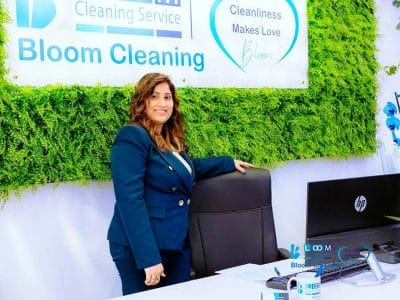 Nishanthi Perera responsabile amministrazione Bloom Cleaning Milano nell’ufficio aziendale, davanti alla scrivania con logo Bloom Cleaning sullo sfondo.