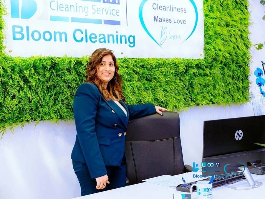 Nishanthi Perera responsabile amministrazione Bloom Cleaning Milano nell’ufficio aziendale, davanti alla scrivania con logo Bloom Cleaning sullo sfondo.