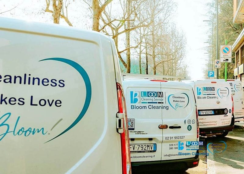 Tre furgoni della Bloom Cleaning parcheggiati lungo una strada alberata esponevano i loghi dell'azienda e lo slogan 