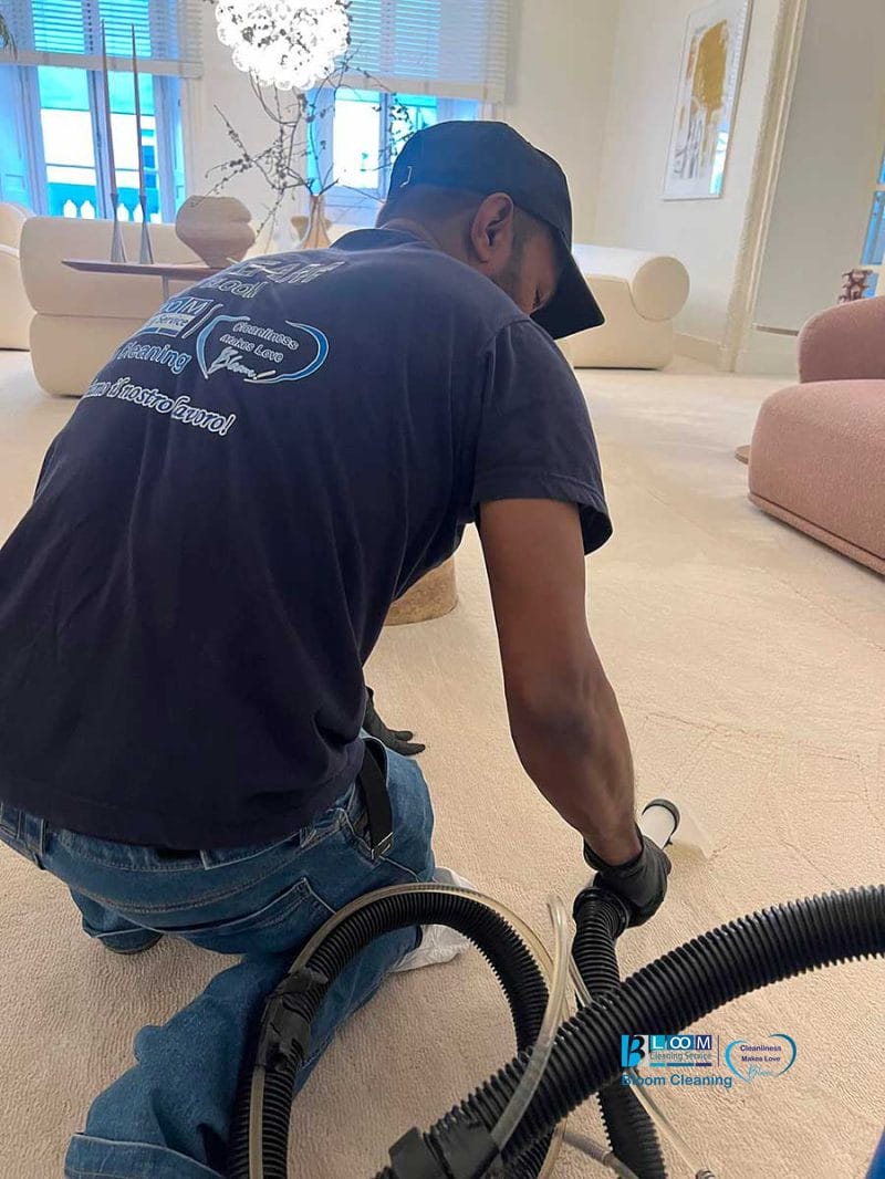 Uomo che pulisce un tappeto chiaro con l'aspirapolvere in un soggiorno moderno e luminoso, a dimostrazione dei risultati impeccabili ottenuti dagli esperti di Pulizia Moquette Milano.